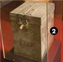 Image of an old ballot box in a perspex case. It appears to be double locked and has the number '8262' on the front.