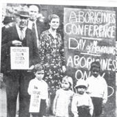 Black and white image of a man holding a small poster that says 'Aborigines claim citizen rights'. Next to him a woman and then a very large placard that says 'Aborigines conference, Day of Mourning, Aborigines only'. Two children, a boy and girl are in the foreground. The little boy has a copy of the same poster as the man's. 
